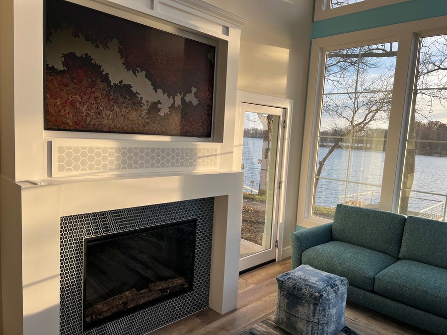 Art mode TV and fireplace beside lakeside windows