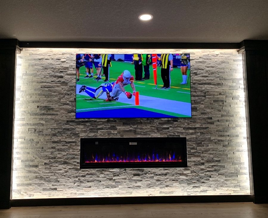 Backlit stacked stone wall with a large TV and linear fireplace