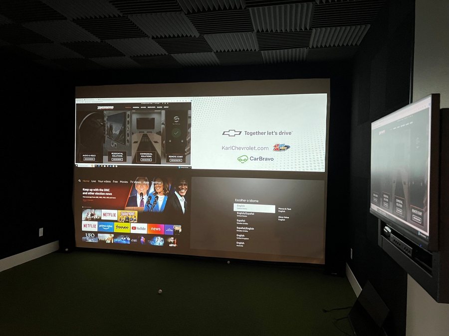 Golf simulator room with projector screen and side TV